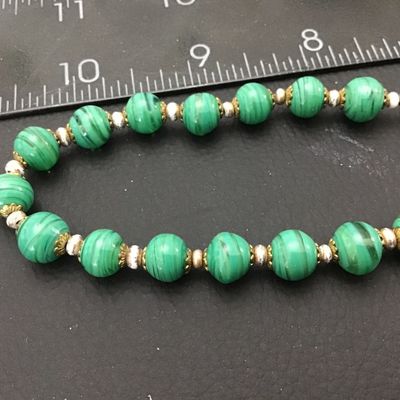 Sale Photo Thumbnail #68: Vintage beaded necklace featuring green striped art glass beads accented with brass filigree caps and small spacer beads. Measures approximately 22 inches end-to-end. Features a brass barrel screw clasp. Good vintage condition with light wear to metal acc