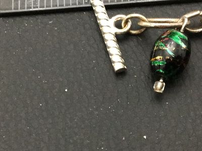 Sale Photo Thumbnail #259: A silver-tone chain bracelet featuring dangling black glass beads decorated with colorful metallic foil flecks/swirls in green, red, and gold tones. Features a textured toggle clasp closure. Measures approximately 7.5 to 8 inches in overall length. Good v