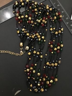 Sale Photo Thumbnail #209: Multi-strand statement necklace by Joan Rivers featuring layered strands of black seed beads interspersed with faceted metallic gold, deep red, and dark green beads. Includes a gold-tone lobster claw clasp with an adjustable extender chain and an oval Joa
