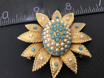Sale Photo Thumbnail #2: A vintage gold-tone flower-shaped brooch featured with a raised domed center set with turquoise blue and faux pearl cabochons. The petals feature a textured gold finish with accenting pearls and blue beads. Measures approximately 2 inches in diameter. The