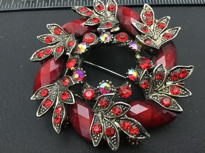 Sale Photo Thumbnail #130: A circular vintage wreath brooch features antiqued silvertone metal detailed with leaf designs. It is set with faceted marquise red cabochons, bright red round rhinestones, and iridescent aurora borealis rhinestones. The pin back and clasp are present on 
