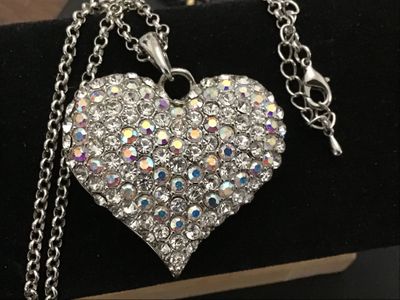 Sale Photo Thumbnail #151: A silver-tone chain necklace featuring a large heart-shaped pendant encrusted with clear and aurora borealis pave rhinestones. The back of the pendant features a openwork filigree heart pattern. Features an adjustable rolo chain with a lobster claw clasp.