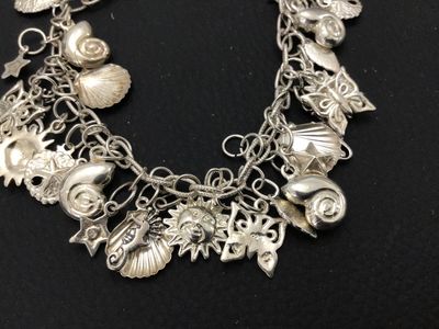Sale Photo Thumbnail #48: A sterling silver charm bracelet featuring various celestial and aquatic/nautical themed charms including suns, butterflies, seashells, starfish, and sand dollars. Multiple charms are marked '925' for sterling silver quality. Features a lobster claw clasp