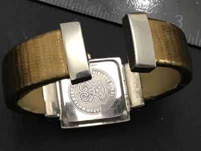 Sale Photo Thumbnail #238: TOUS ladies quartz wrist watch featuring a square face with the iconic TOUS bear graphic on the dial and dangling bear charm. Features a stainless steel back, Japan quartz movement, and an open cuff-style band with textured bronze/gold tone finish. Light 