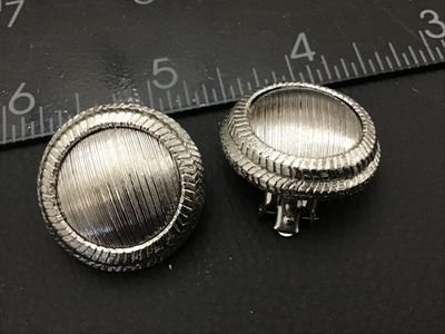Sale Photo Thumbnail #243: Pair of vintage silver-tone clip-on earrings featuring a textured dome center and chevron patterned outer rim. Each clip-on earring measures approximately 1 inch in diameter. In good condition with functional clip backs and light vintage wear.