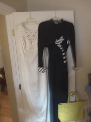 Sale Photo Thumbnail #21: Pair of vintage formal dresses, including a sleeveless white lace gown and a black long-sleeve evening dress hanging on a door, along with a yellow woven tote bag.