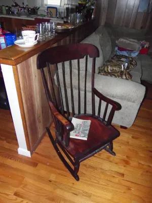 Sale Photo Thumbnail #7: Vintage dark mahogany wooden rocking chair with spindled back rests on a hardwood floor.