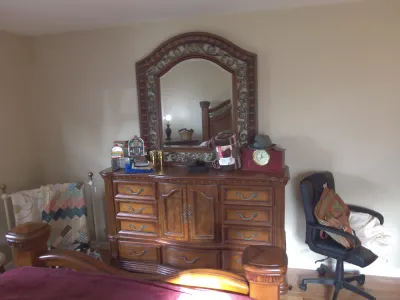 Sale Photo Thumbnail #25: Traditional wooden bedroom set featuring a multi-drawer dresser with an arched ornate attached mirror, a matching bed frame, and an office chair.