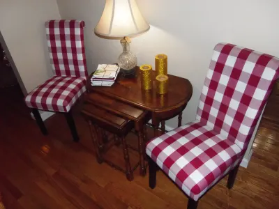 Sale Photo Thumbnail #11: Pair of red and white gingham-upholstered accent chairs flanking a wooden nesting table set with a glass table lamp.