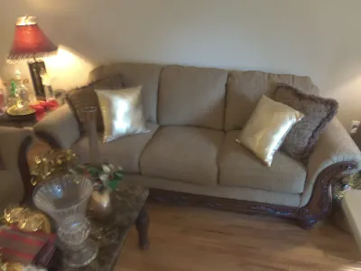 Sale Photo Thumbnail #15: Traditional tan upholstered three-cushion sofa featuring carved wood trim and rolled arms, styled with decorative throw pillows.