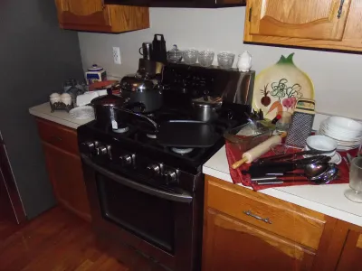Sale Photo Thumbnail #10: Kitchen counter and gas range featuring an assortment of cookware, including stainless steel pots, a cast iron griddle, glass glassware, a box grater, and ceramic dishware.
