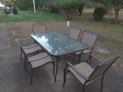 Sale Photo Thumbnail #4: Seven-piece outdoor patio dining set featuring a metal-framed glass-top rectangular table with six matching tan sling armchairs.