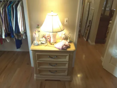 Sale Photo Thumbnail #19: Light oak three-drawer nightstand topped with a illuminated ceramic table lamp and decorative accessories.