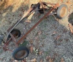 Vintage rusted go-kart metal frame with four rubber wheels, showing heavy wear and surface oxidation.