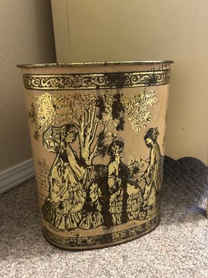 Vintage embossed tin wastebasket depicting Victorian-era women in a garden setting, showing age-related wear and patina.