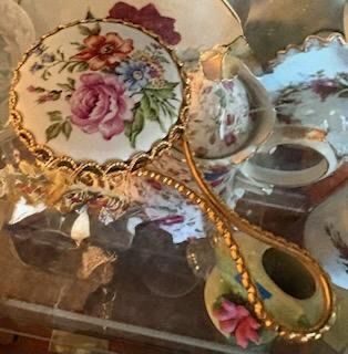 Vintage hand mirror featuring an ornate gold-tone filigree frame and a hand-painted porcelain back with floral motifs.