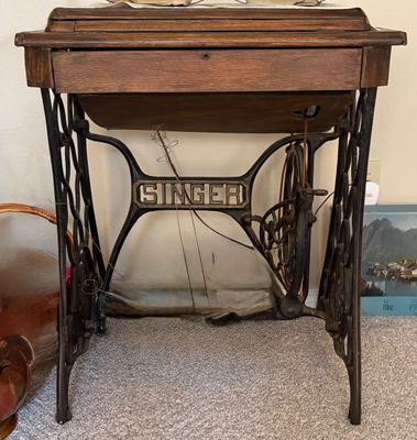 Vintage Singer treadle sewing machine cabinet with a cast iron base and a dark wood drop-leaf table top.