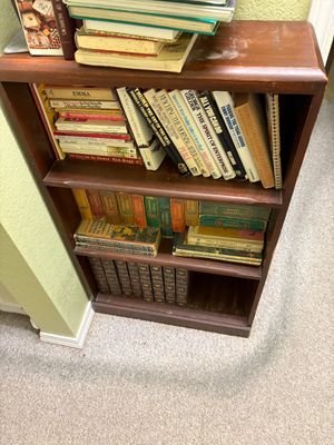 Small three-tier wooden bookcase filled with a variety of vintage paperbacks, hardcovers, and encyclopedia sets.