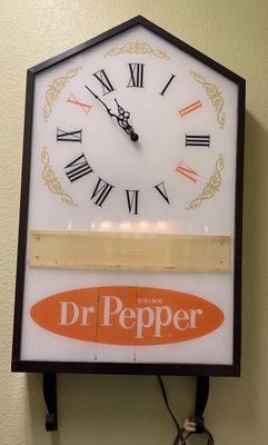 Vintage Dr Pepper illuminated wall clock featuring Roman numerals with highlighted 10, 2, and 4 hour markers and a house-shaped dark frame.