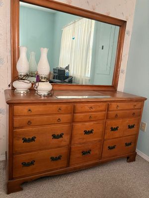 Vintage early American-style wooden double dresser with matching framed mirror and brass hardware, accompanied by a pair of white hobnail...