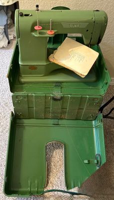 Vintage green Elna Supermatic sewing machine with its original metal carrying case and instruction manual.