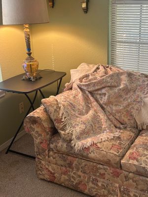 Floral upholstered sofa draped with fringed woven throws, set alongside an ornate vintage table lamp on a modern side table.