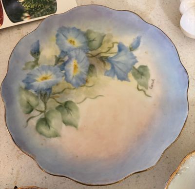 Hand-painted porcelain decorative plate featuring blue morning glory flowers with a scalloped gold-trimmed edge, signed "Carol".