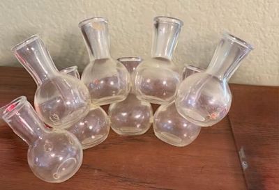 Collection of small vintage clear glass apothecary bottles or bud vases with bulbous bases and flared rims.