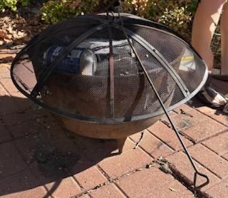 Round metal outdoor fire pit featuring a mesh spark screen cover and an included poker tool.
