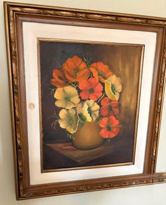 Vintage framed oil painting depicting a floral still life of orange and yellow flowers in a vase, housed in an ornate carved wooden frame.