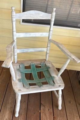 Vintage white-painted wooden ladderback armchair featuring turned posts and green webbing across the open seat frame.