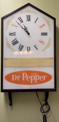 Vintage illuminated Dr Pepper electric wall clock featuring a house-shaped frame, Roman numeral face with '10-2-4' numbers...