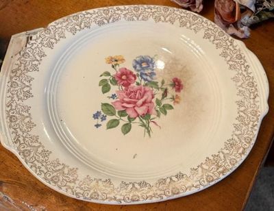 Vintage ceramic cake plate featuring a central floral bouquet pattern, ornate gold filigree rim, and integrated side handles.