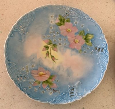 Hand-painted antique porcelain plate featuring pink wild roses on a soft blue background with embossed reticulated border details.