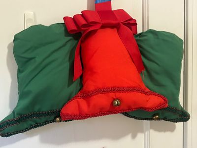 Handmade Christmas door hanger featuring stuffed fabric bells in red and green, trimmed with gimp braid, small jingle bells, and a red bow.