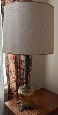 Vintage table lamp featuring an amber marigold carnival glass floral font, ornate cast metal column base, and a large beige drum shade.