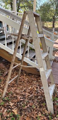 Vintage aluminum step ladder showing age-related wear, weathering, and patina, standing outdoors near a wooden deck.