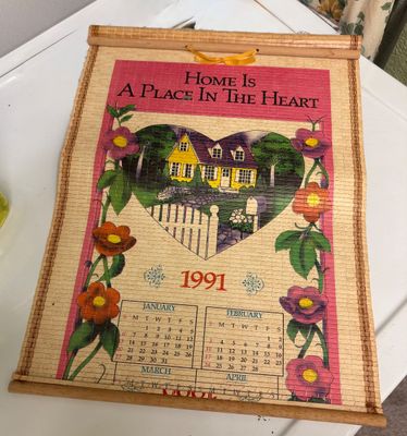 Vintage 1991 bamboo slat scroll wall calendar featuring a house graphic and the phrase "Home Is A Place In The Heart".