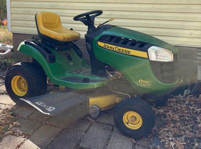 John Deere D110 riding lawn mower featuring a green and yellow body, high-back vinyl seat, and side discharge deck.