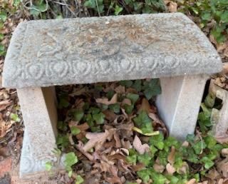 Weathered cast concrete garden bench featuring embossed floral and egg-and-dart relief details along the top surface and edge.