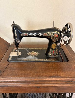 Antique Singer treadle sewing machine with ornate gold and colorful floral decals, mounted in a wooden cabinet.