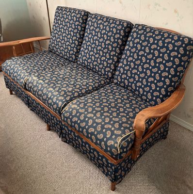 Vintage three-seat sofa with blue and tan paisley upholstery and exposed wooden armrests. The fabric shows minor wear and fraying along...