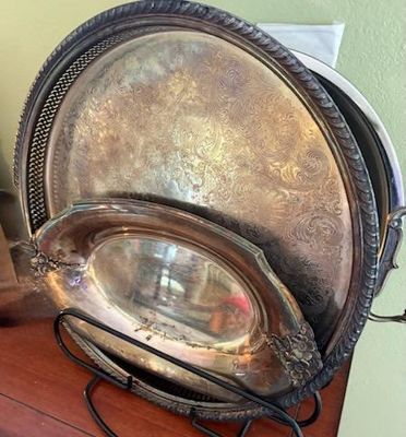Collection of vintage silver-plated serveware, including an etched round tray and small oval dish displayed on a wire rack.