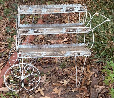 Vintage white wrought iron three-tier plant stand cart featuring decorative leaf accents and scrollwork wheels.
