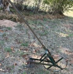 Vintage iron walk-behind garden cultivator with a single spoked front wheel and a long handle.