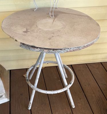 Vintage white metal bistro table with a round tabletop showing heavy wear and weather damage.