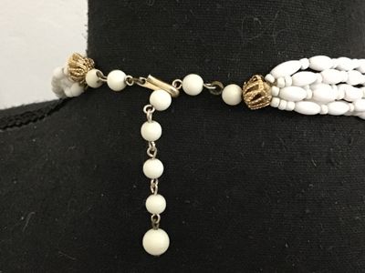 Sale Photo Thumbnail #171: Vintage multi-strand statement necklace featuring white rice/oval-shaped molded  glass beads. Finished with decorative gold-tone filigree end caps and an adjustable hook closure with extension chain. Marked 'JAPAN' on the hook clasp. In good vintage condi