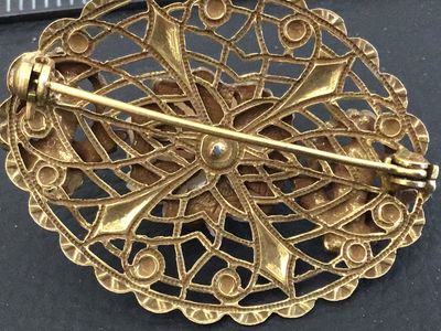 Sale Photo Thumbnail #43: An intricate oval vintage brooch featuring detailed gold-tone filigree metalwork, a central carved faux-coral or resin rose bloom, and two cherub/putti figures on either side. Features a rollover safety clasp on the reverse. Shows minor signs of vintage w