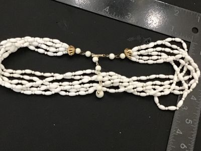 Sale Photo Thumbnail #168: Vintage multi-strand statement necklace featuring white rice/oval-shaped molded  glass beads. Finished with decorative gold-tone filigree end caps and an adjustable hook closure with extension chain. Marked 'JAPAN' on the hook clasp. In good vintage condi