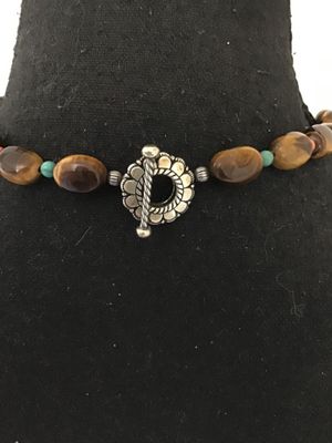 Sale Photo Thumbnail #22: A beaded gemstone necklace featuring smooth, polished tiger's eye oval beads accented with small turquoise and red/coral-tone spacer beads and silver-tone fluted metal spacers. Finished with a decorative silver-tone toggle closure clasp. In good pre-owned